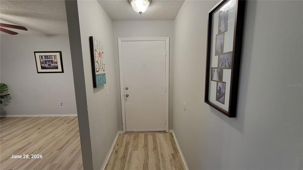 An entryway with light wood flooring, a white front door, and framed wall art — 4136 PERSHING POINTE PLACE UNIT 5, ORLANDO, FL