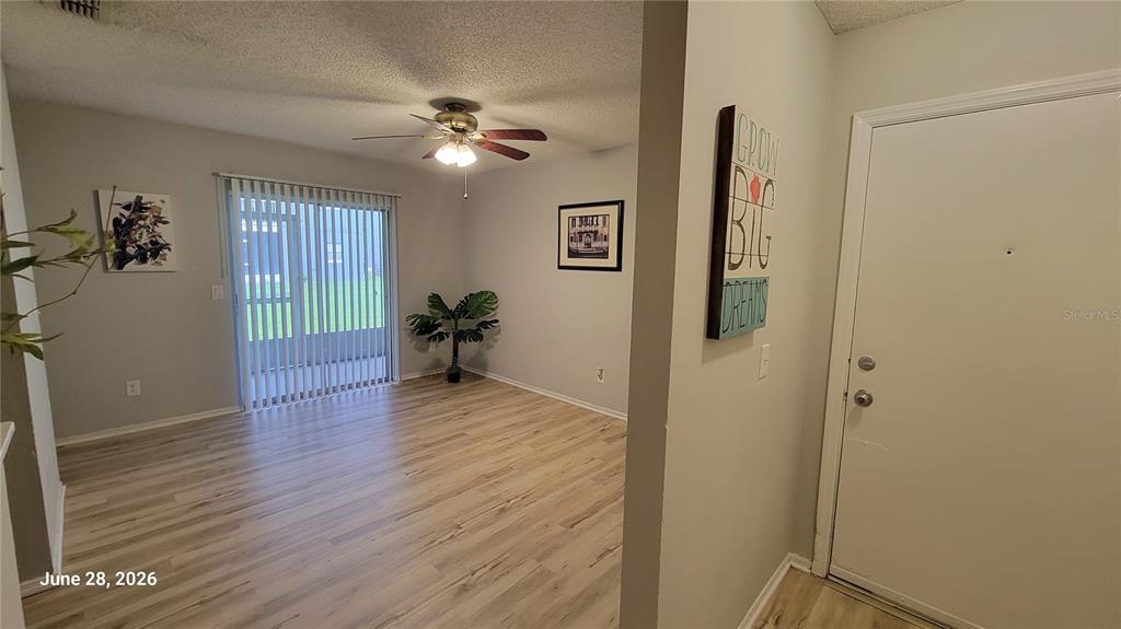 A living room with light wood-look flooring, a ceiling fan, and a sliding glass door — 4136 PERSHING POINTE PLACE UNIT 5, ORLANDO, FL