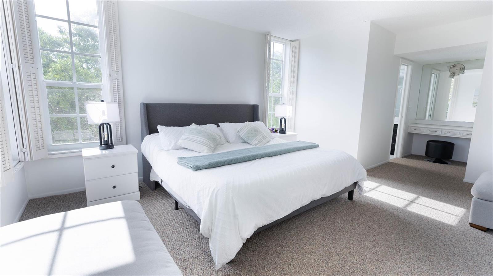 A bedroom features a gray upholstered bed, white nightstands, and a vanity area with mirrors — 3100 N Course Lane # 510, Pompano Beach FL 33069, POMPANO BEACH, FL
