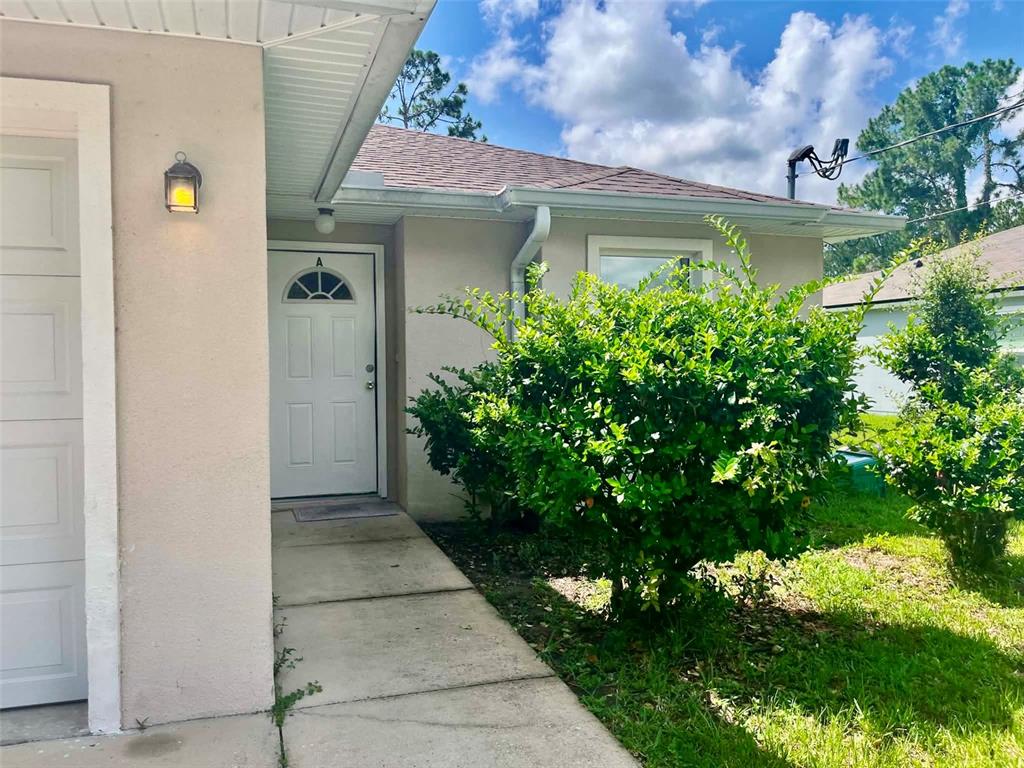 A concrete walkway leads to the front door of a house with a beige exterior — 6 PLEASANT LANE, PALM COAST, FL