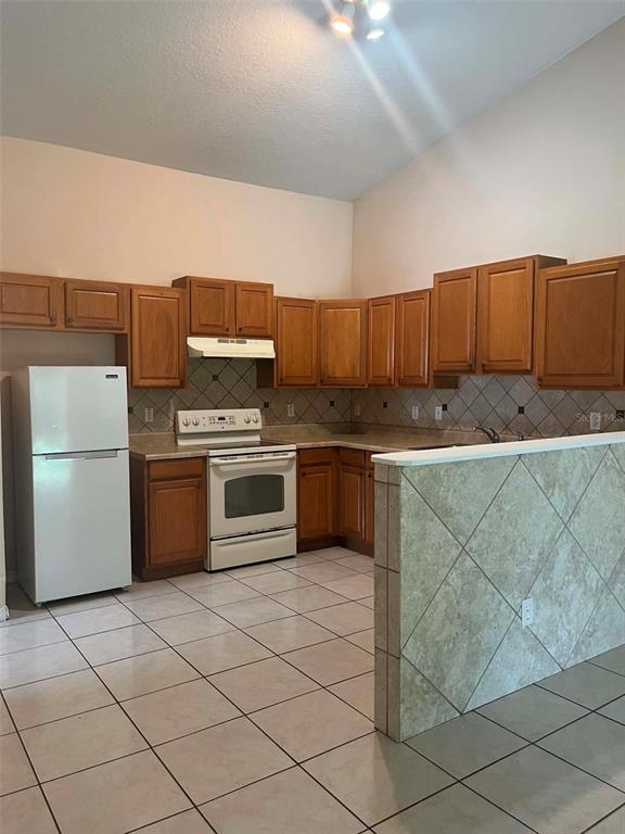 A kitchen features wood cabinets, white appliances, tiled countertops, and light-colored floor tiles — 6 PLEASANT LANE, PALM COAST, FL