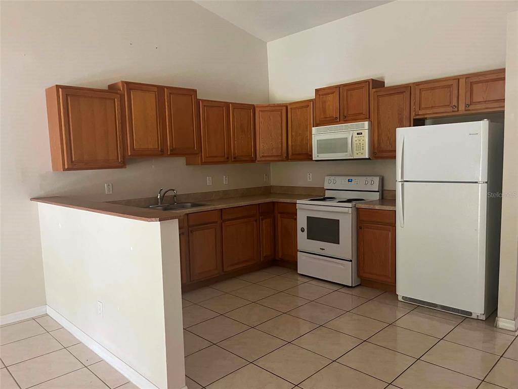 A kitchen features wooden cabinets, white appliances, a tiled floor, and a peninsula counter — 6 PLEASANT LANE, PALM COAST, FL