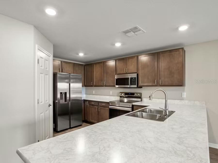 A kitchen with wood cabinets, stainless steel appliances, and a white marble-patterned countertop island — 349 WHARF WAY, WINTER HAVEN, FL