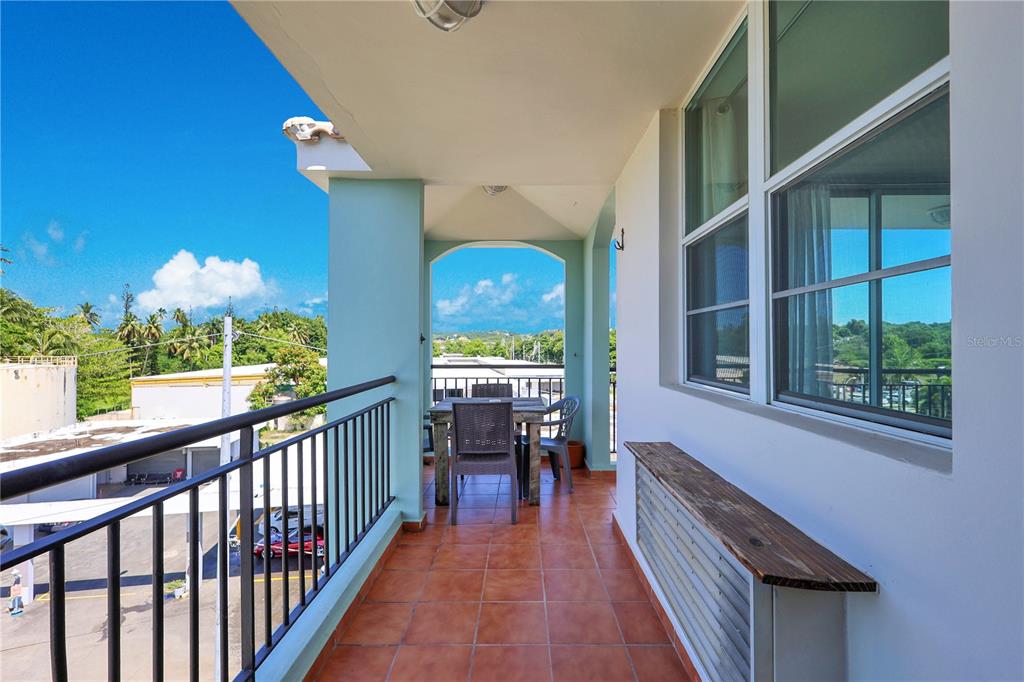 A covered balcony features tiled flooring, a dining set, and a wooden shelf — 115 115 UNIT 401, RINCON, PR
