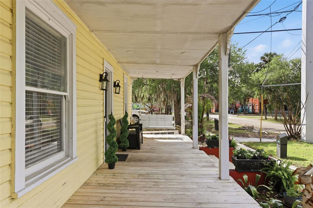 A wooden front porch with a swing, potted plants, and yellow siding on a house — 209 E 5TH STREET, SANFORD, FL