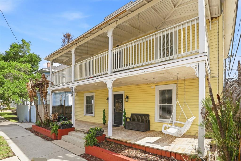 A two-story yellow house features a wooden front porch with a swing and balcony — 209 E 5TH STREET, SANFORD, FL