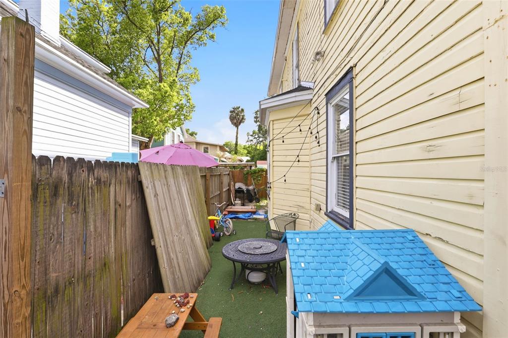 A narrow side yard features a wooden fence, artificial turf, a table, and a playhouse — 209 E 5TH STREET, SANFORD, FL