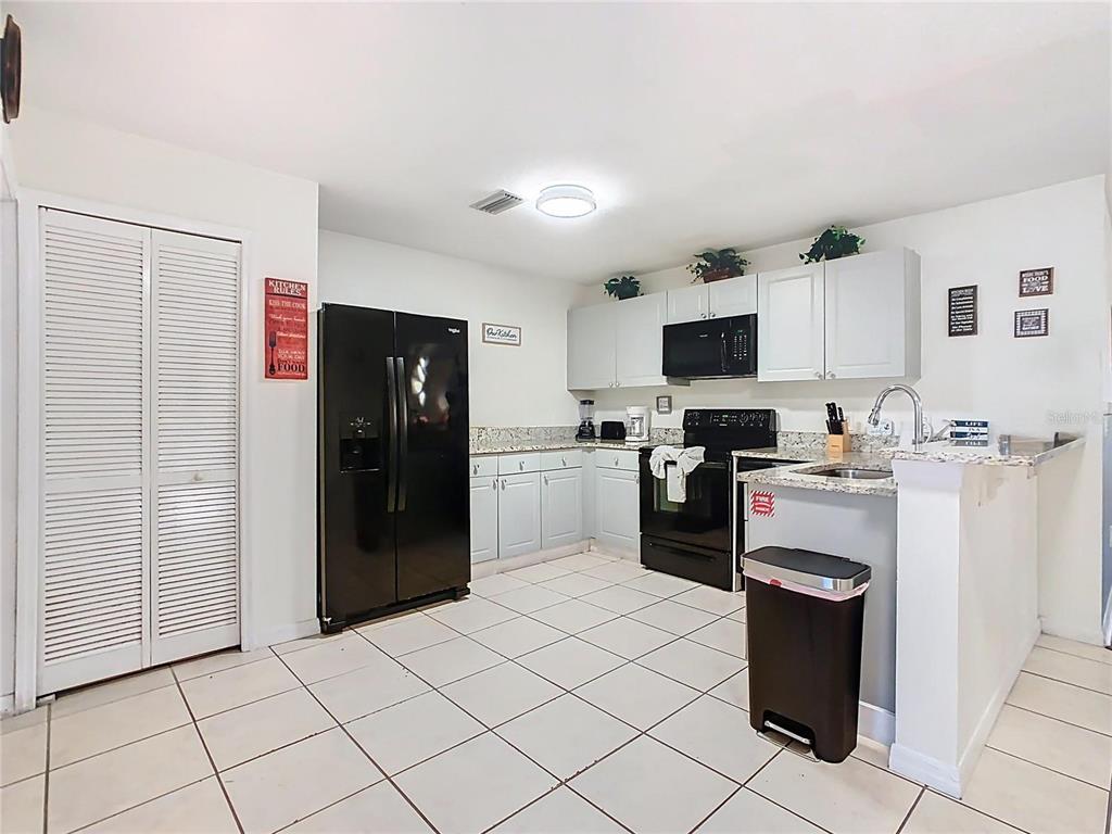 A kitchen with light gray cabinets, black appliances, granite countertops, and white tile flooring — 2810 CLUB CORTILE CIRCLE UNIT A, KISSIMMEE, FL