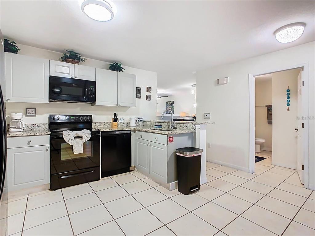 A kitchen features light gray cabinets, black appliances, granite countertops, and white tile flooring — 2810 CLUB CORTILE CIRCLE UNIT A, KISSIMMEE, FL
