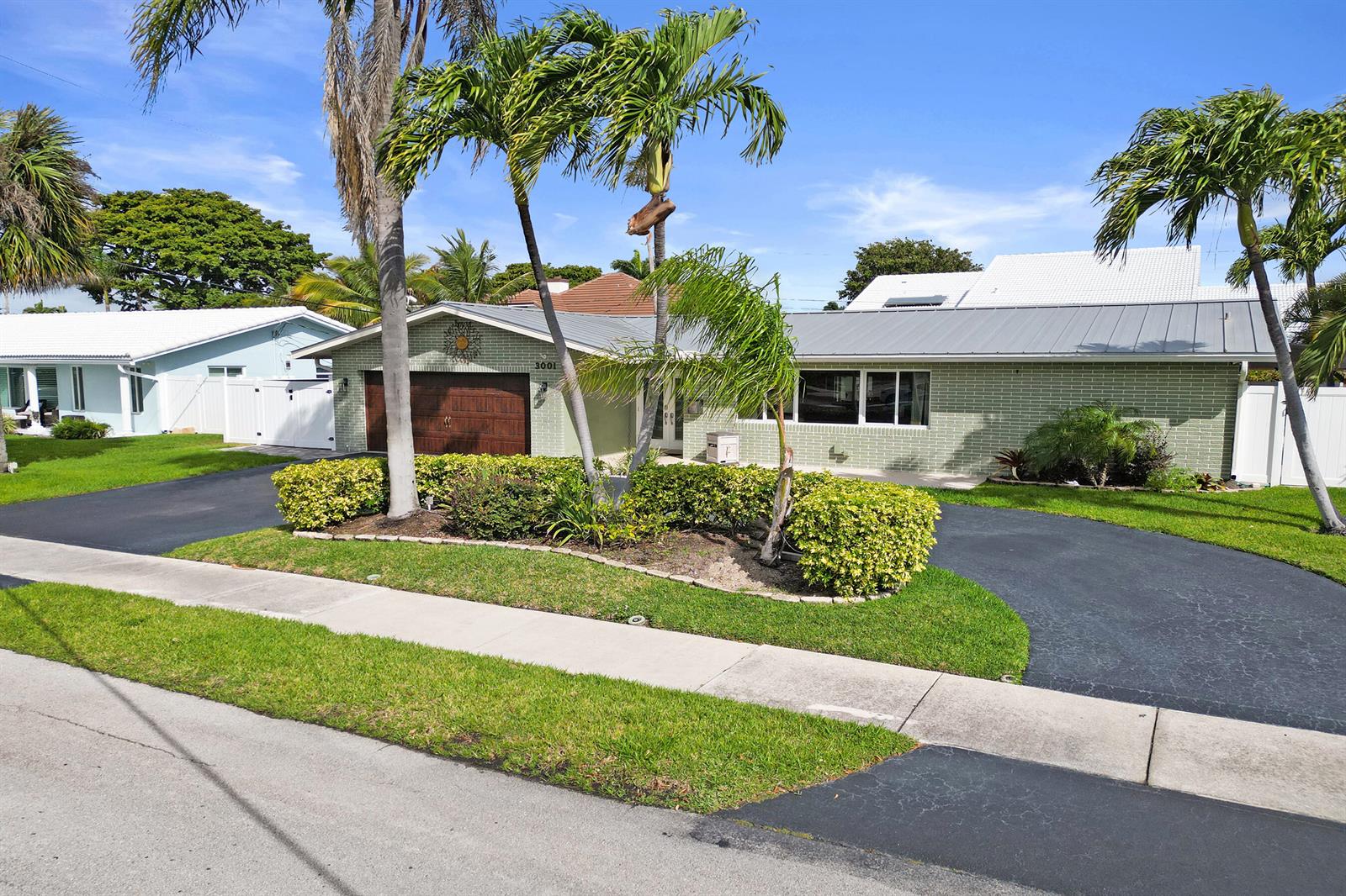 A single-story house with a brick facade, dark wood garage door, and palm trees at dusk — 3001 NE 45th Street, Lighthouse Point FL 33064, LIGHTHOUSE POINT, FL