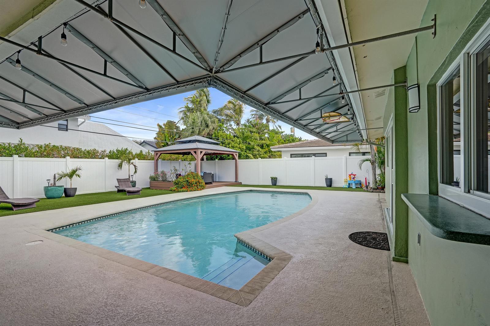 A white single-story house with a metal roof, dark garage door, and palm trees — 3001 NE 45th Street, Lighthouse Point FL 33064, LIGHTHOUSE POINT, FL
