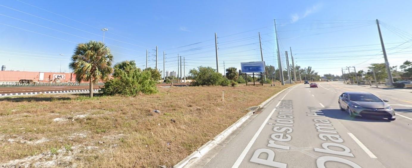 A vacant grassy lot sits next to a road with a billboard and railroad tracks — 0 Dixie Hwy, Riviera Beach FL 33404, RIVIERA BEACH, FL