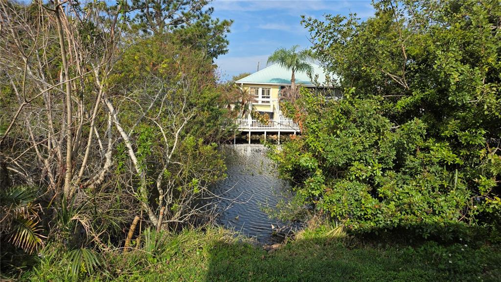 A yellow house with a metal roof sits behind trees along a narrow canal — 622 GOODWIN AVENUE, NEW SMYRNA BEACH, FL
