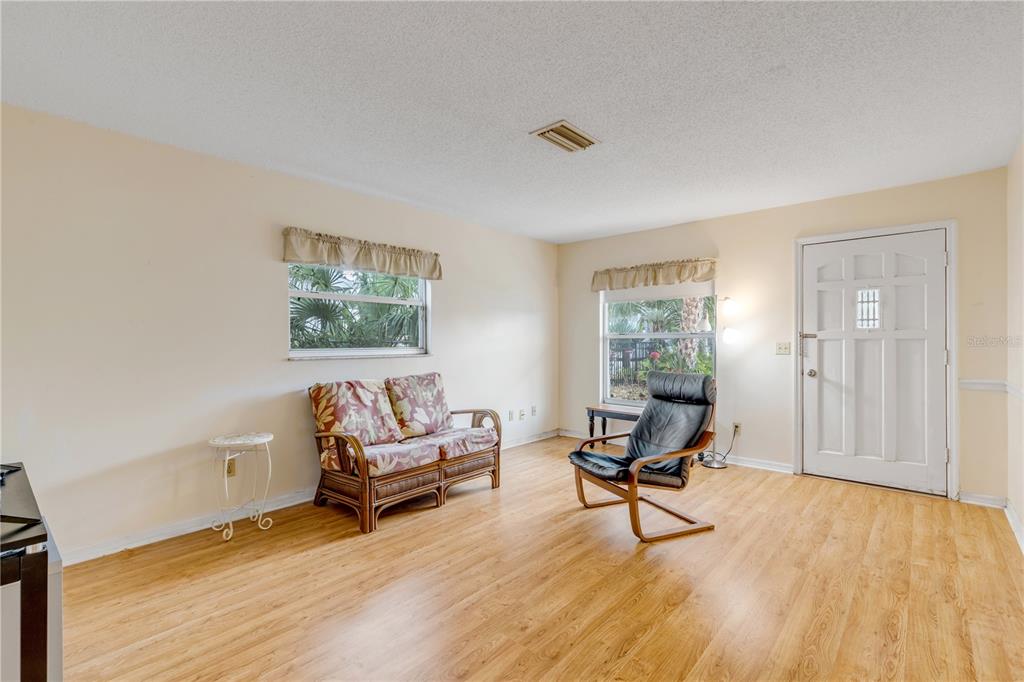 A living room features light wood-look flooring, a floral loveseat, a black armchair, and windows — 622 GOODWIN AVENUE, NEW SMYRNA BEACH, FL