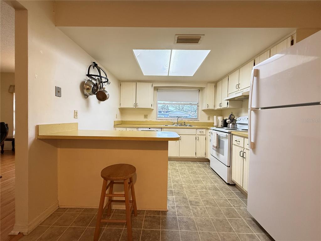 A kitchen features white cabinets, a breakfast bar, a white refrigerator, and a skylight — 622 GOODWIN AVENUE, NEW SMYRNA BEACH, FL