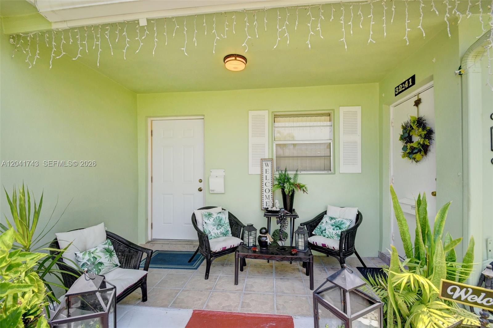 A covered porch features light green walls, tiled flooring, and a seating area with wicker chairs — 3241 Ridge Hill Rd, Boynton Beach FL 33435, BOYNTON BEACH, FL