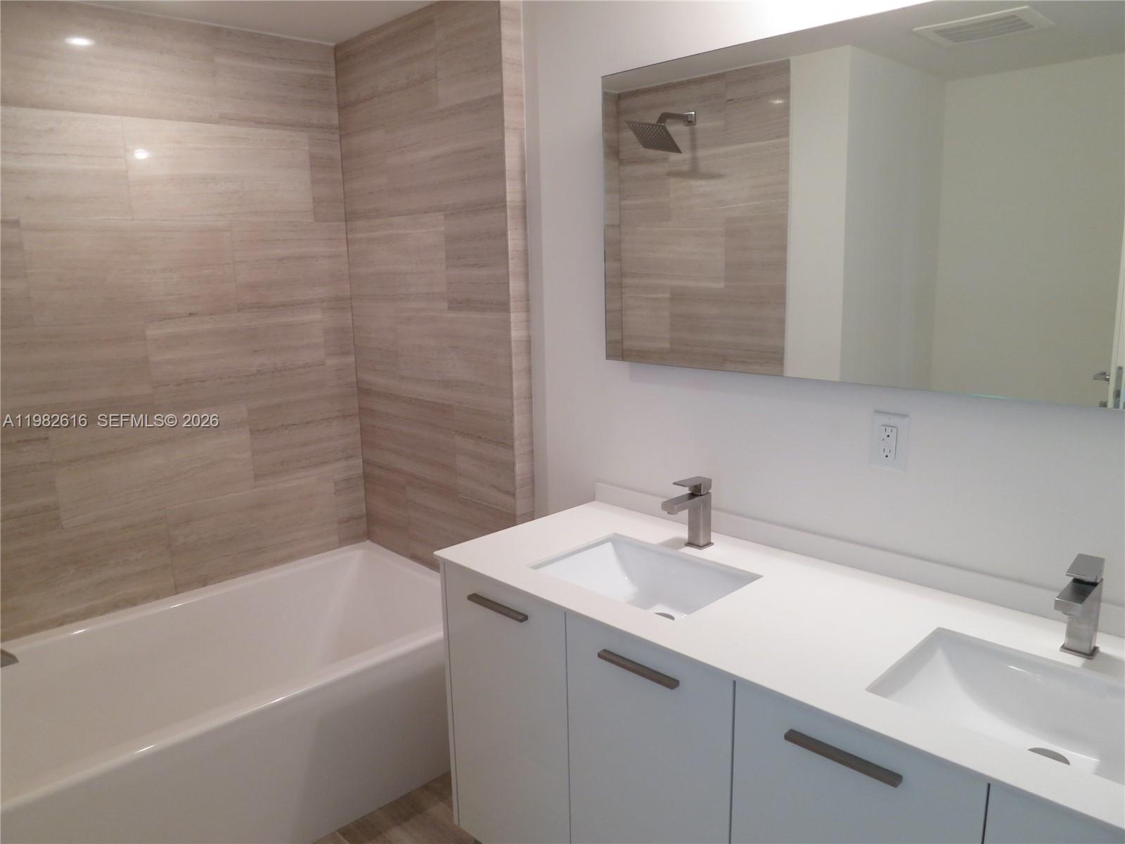 A modern bathroom features a white double vanity, a bathtub, and light-toned tiled walls — 1300 BRICKELL BAY DR # 1100, Miami FL 33131, MIAMI, FL