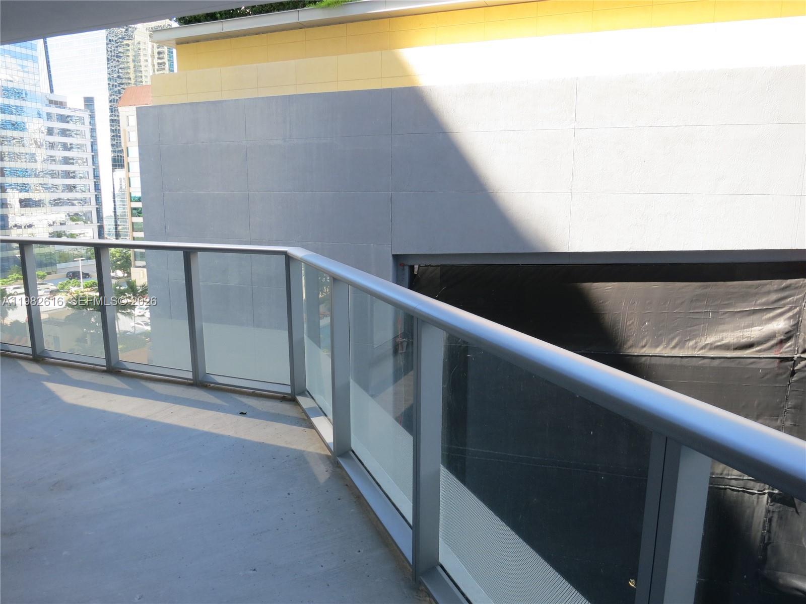 A balcony with a glass railing overlooks a city street and a neighboring building — 1300 BRICKELL BAY DR # 1100, Miami FL 33131, MIAMI, FL