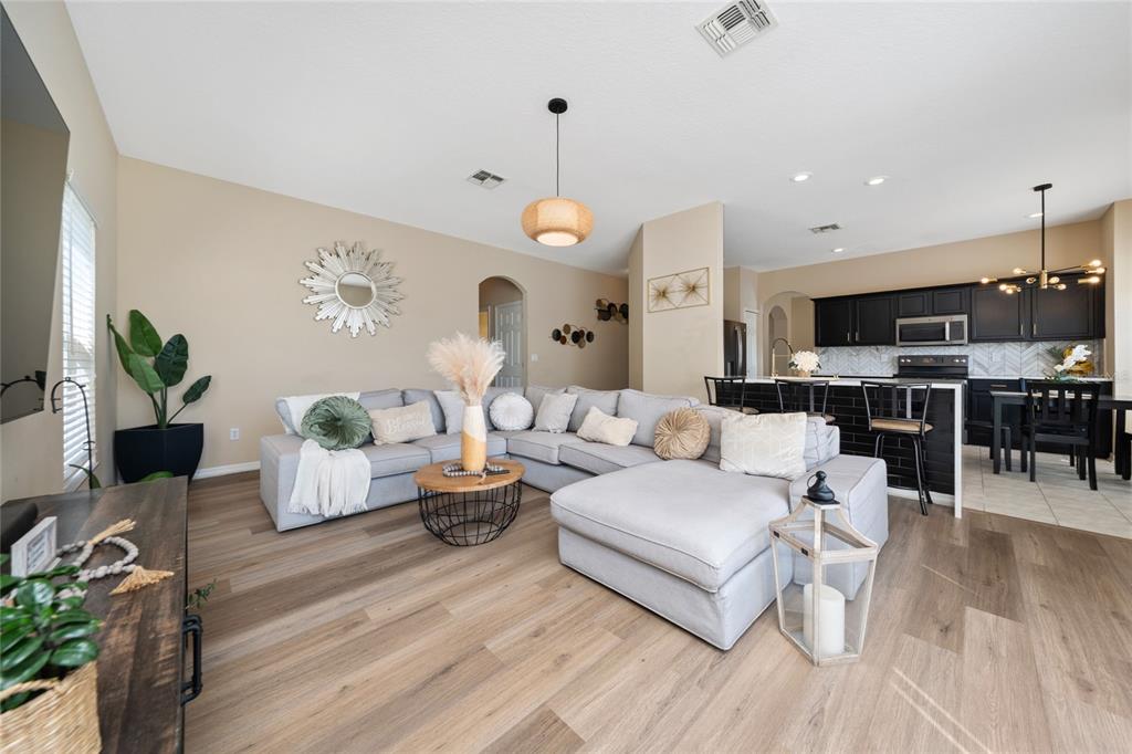 A living room with a light gray sectional sofa, wood-look flooring, and an open kitchen — 2764 PATRICIAN CIRCLE, KISSIMMEE, FL