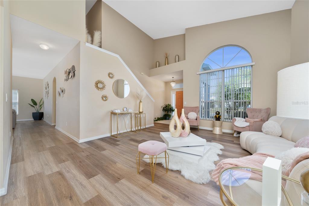 A bright living room features high ceilings, wood-look flooring, and a large arched window — 2764 PATRICIAN CIRCLE, KISSIMMEE, FL