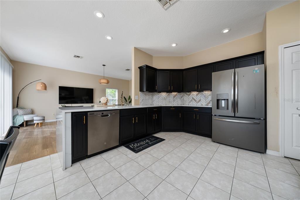 A kitchen with black cabinets, stainless steel appliances, and a tiled floor opens to a living area — 2764 PATRICIAN CIRCLE, KISSIMMEE, FL