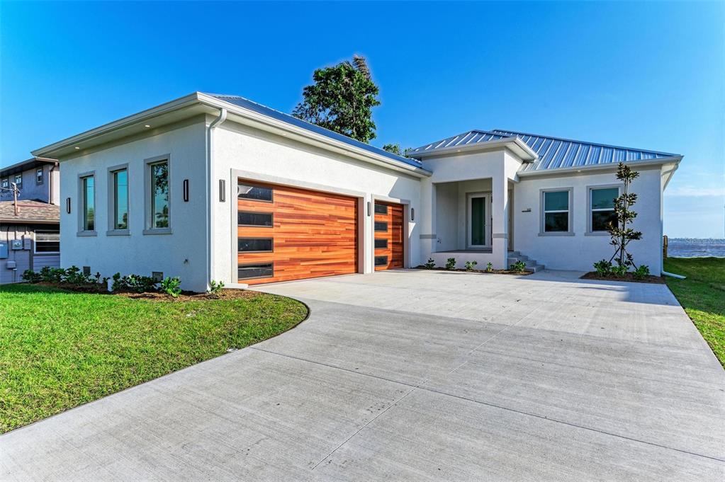 A modern white house with a metal roof and wood-paneled garage doors — 112 NORTHSHORE TERRACE, PUNTA GORDA, FL
