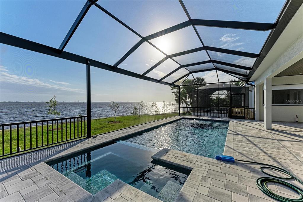 A screened-in pool and spa overlook a large body of water from a paved patio — 112 NORTHSHORE TERRACE, PUNTA GORDA, FL