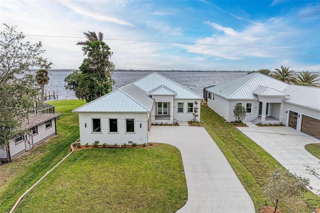 An aerial view shows two modern white houses with metal roofs beside a large body of water — 112 NORTHSHORE TERRACE, PUNTA GORDA, FL