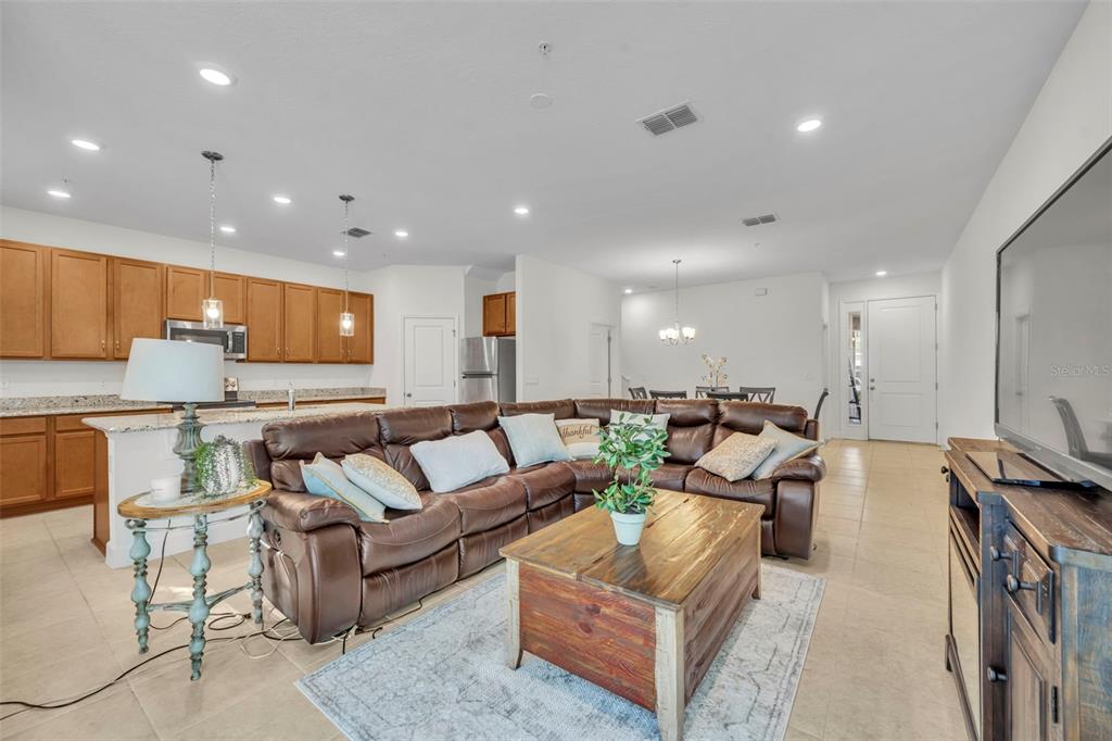 A living room with a brown leather sectional, wooden coffee table, and an open kitchen — 986 GRAND WILDMERE COVE, LONGWOOD, FL
