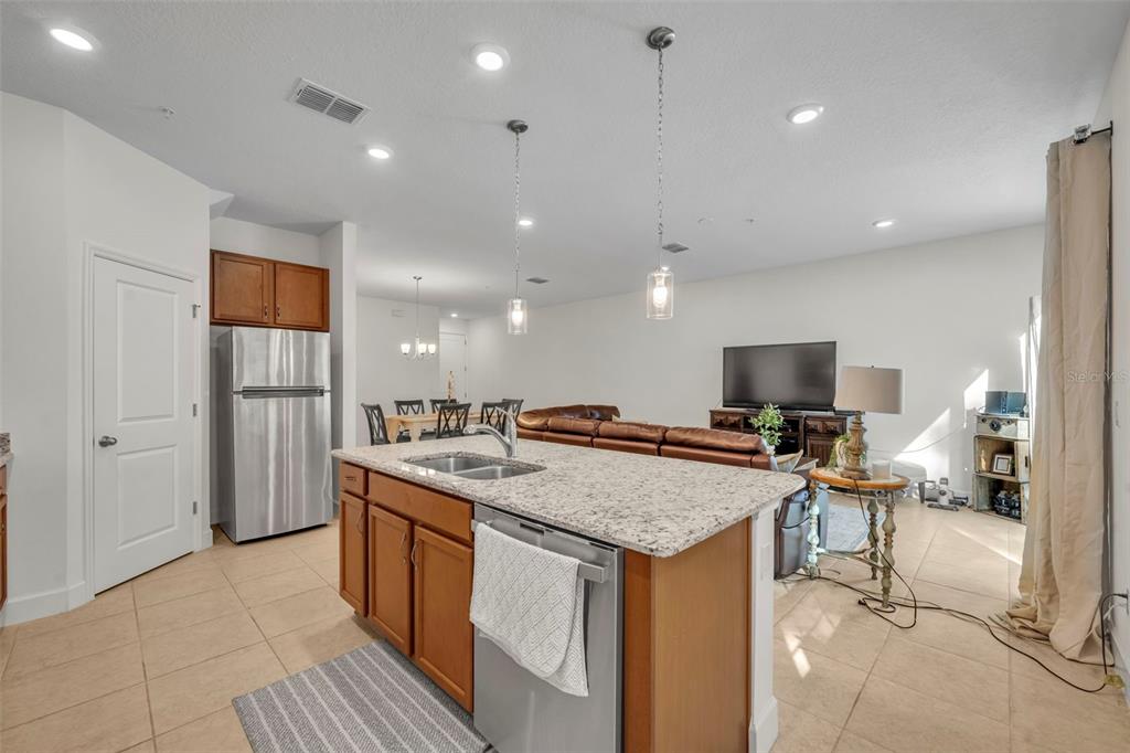 A kitchen island with granite countertops sits in front of an open-concept living and dining area — 986 GRAND WILDMERE COVE, LONGWOOD, FL