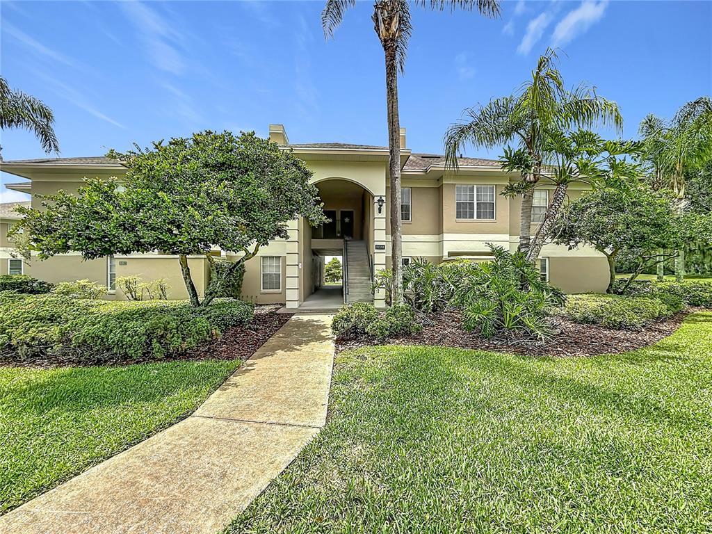 A two-story apartment building exterior features a central staircase, palm trees, and landscaped lawn — 704 EAGLE POND DRIVE UNIT 704, WINTER HAVEN, FL