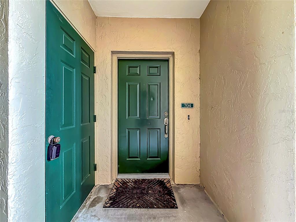 A green front door with a "704" sign sits at the end of a covered entryway — 704 EAGLE POND DRIVE UNIT 704, WINTER HAVEN, FL