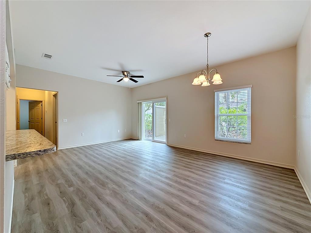 An open-concept living and dining area features wood-look flooring, a ceiling fan, and sliding doors — 704 EAGLE POND DRIVE UNIT 704, WINTER HAVEN, FL