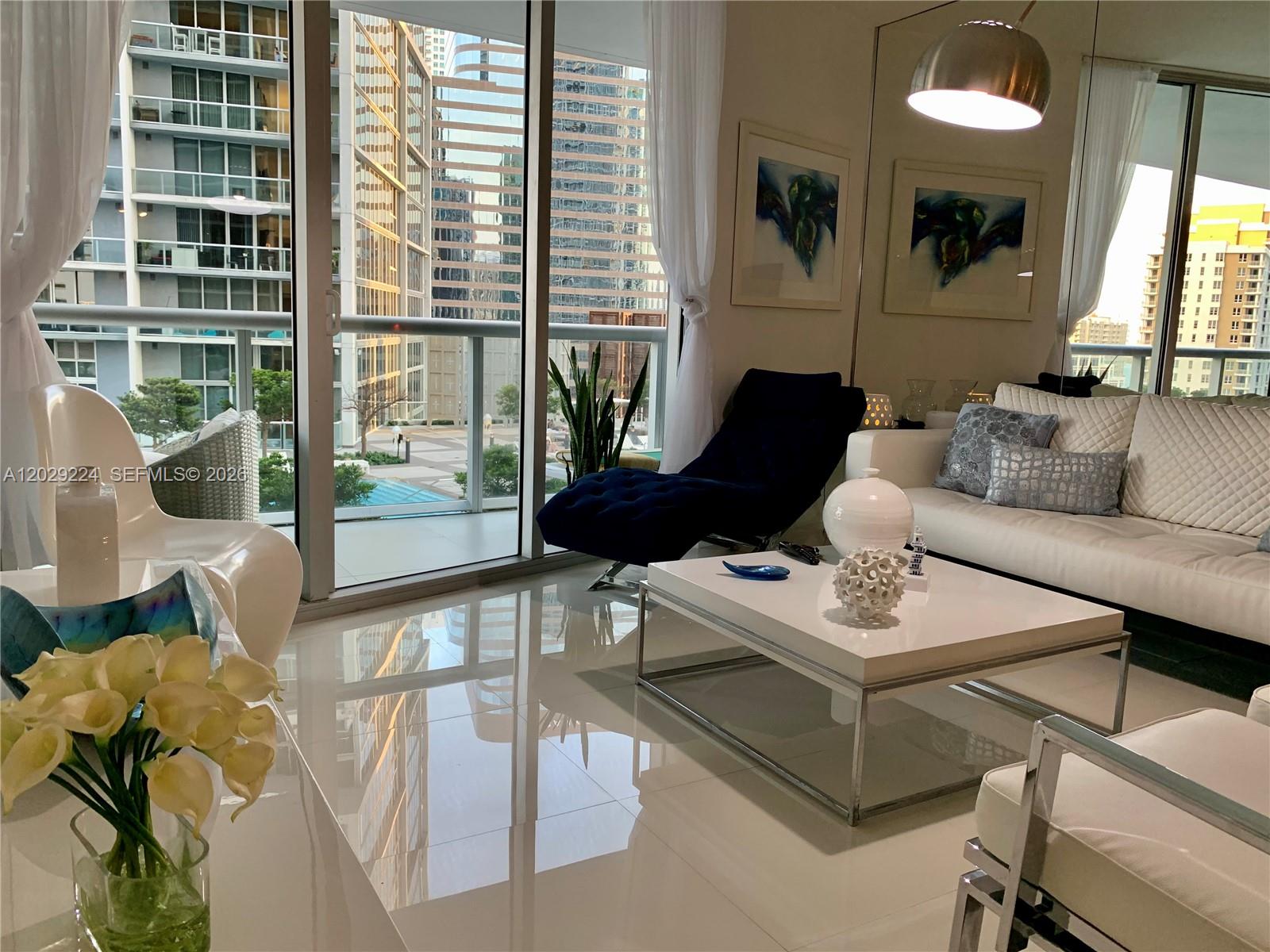 A modern living room features white tile floors, a white sofa, and floor-to-ceiling windows — 475 Brickell Ave # 1611, Miami FL 33131, MIAMI, FL