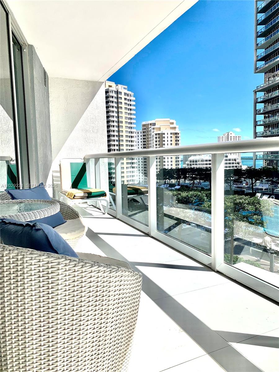 A balcony with wicker chairs overlooks a swimming pool and surrounding high-rise buildings — 475 Brickell Ave # 1611, Miami FL 33131, MIAMI, FL