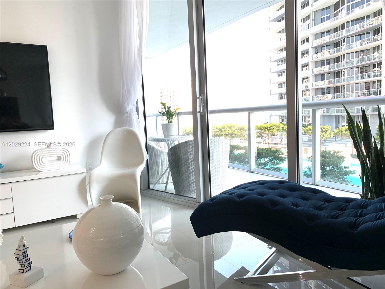 A modern living room features a blue chaise lounge, white furniture, and a balcony view — 475 Brickell Ave # 1611, Miami FL 33131, MIAMI, FL
