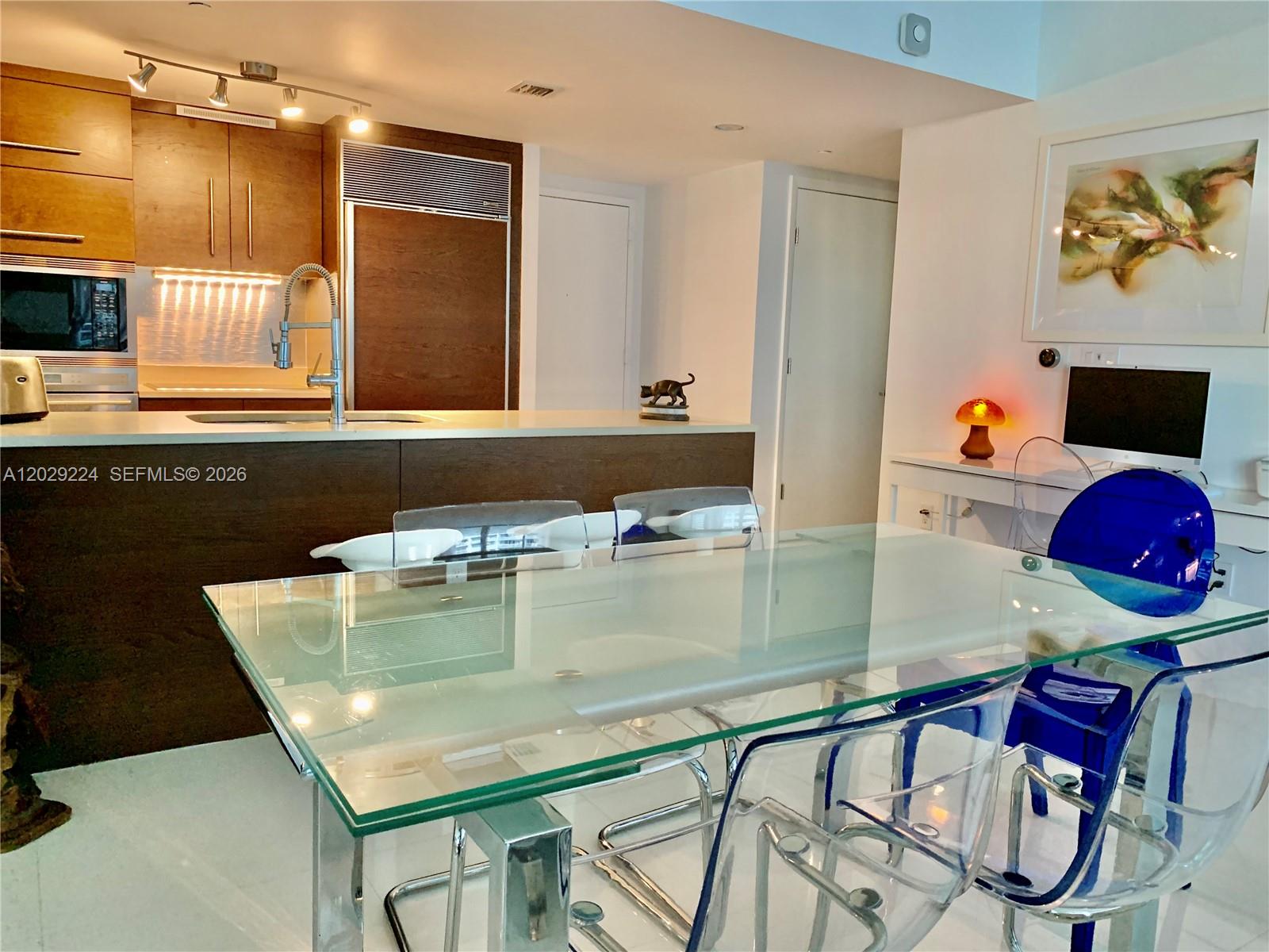 A modern kitchen with wood cabinetry and a glass dining table with transparent chairs — 475 Brickell Ave # 1611, Miami FL 33131, MIAMI, FL
