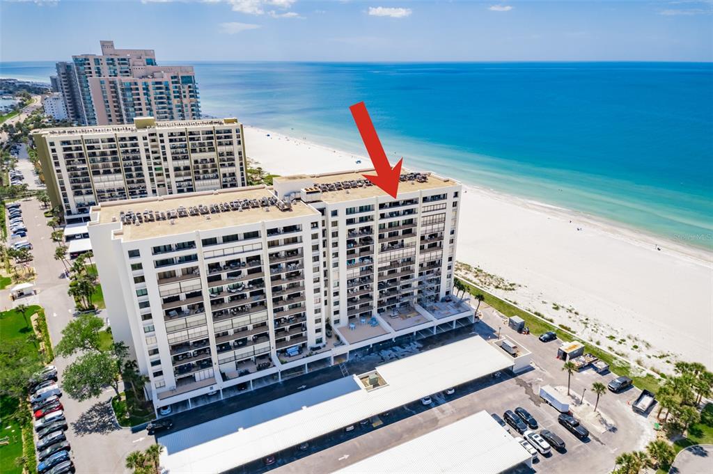 An aerial view shows a beachfront condominium building with a red arrow pointing toward balconies — 1460 GULF BOULEVARD UNIT 1205, CLEARWATER BEACH, FL