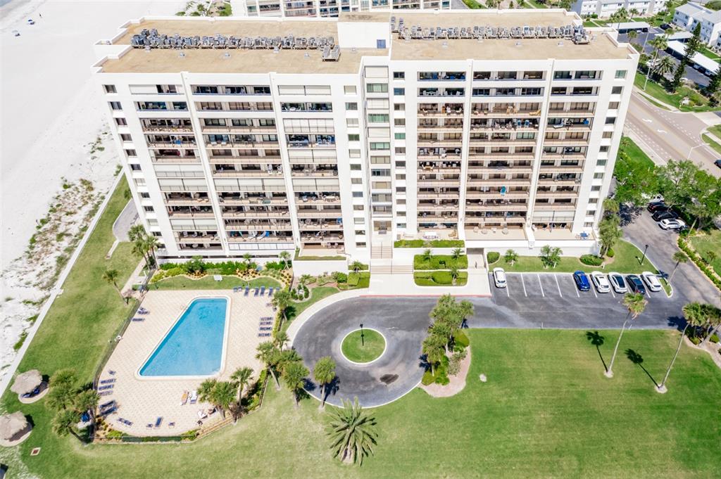 An aerial view shows a multi-story beachfront condominium building with a pool and parking lot — 1460 GULF BOULEVARD UNIT 1205, CLEARWATER BEACH, FL