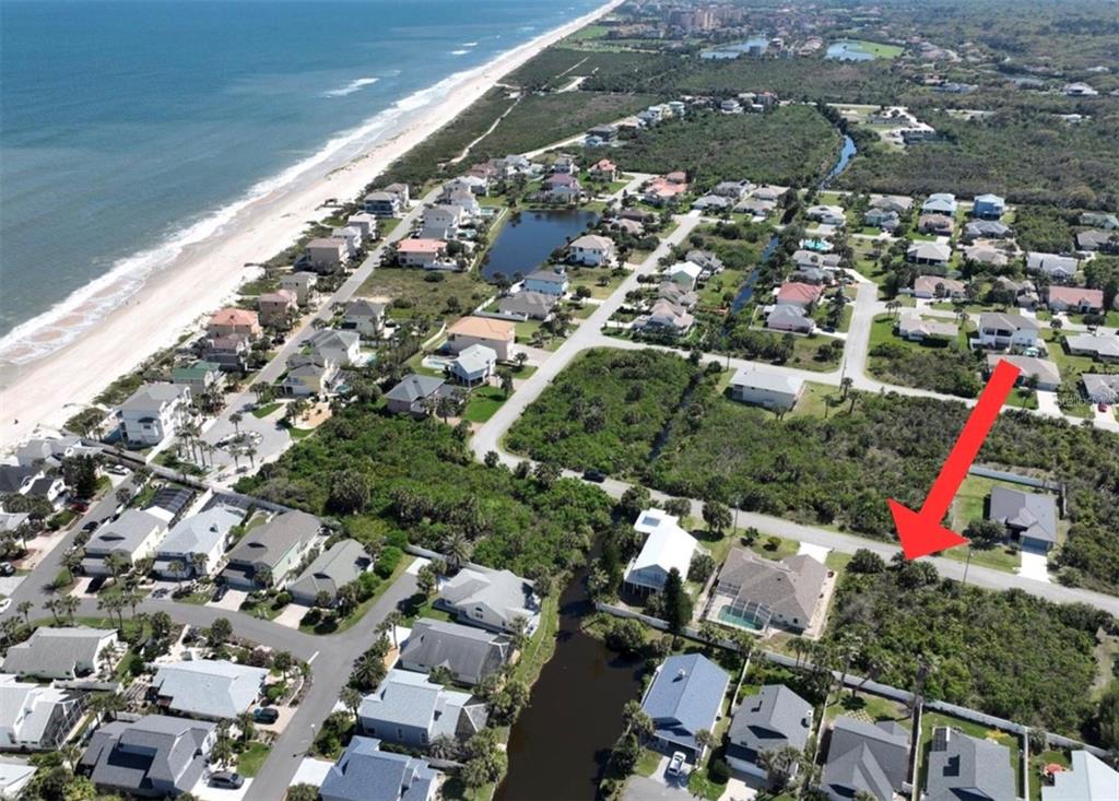 An aerial view shows a coastal neighborhood with a red arrow pointing to a vacant lot — 11 MAHOE DRIVE N, PALM COAST, FL