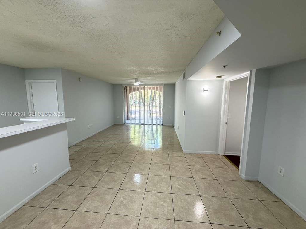 An empty living area features light-colored tile flooring, white walls, and sliding glass doors — 2173 Renaissance Blvd # 101, Miramar FL 33025, MIRAMAR, FL