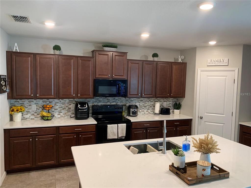 A kitchen features dark wood cabinets, white countertops, a central island, and a mosaic backsplash — 10460 CARLOWAY HILLS DRIVE, WIMAUMA, FL