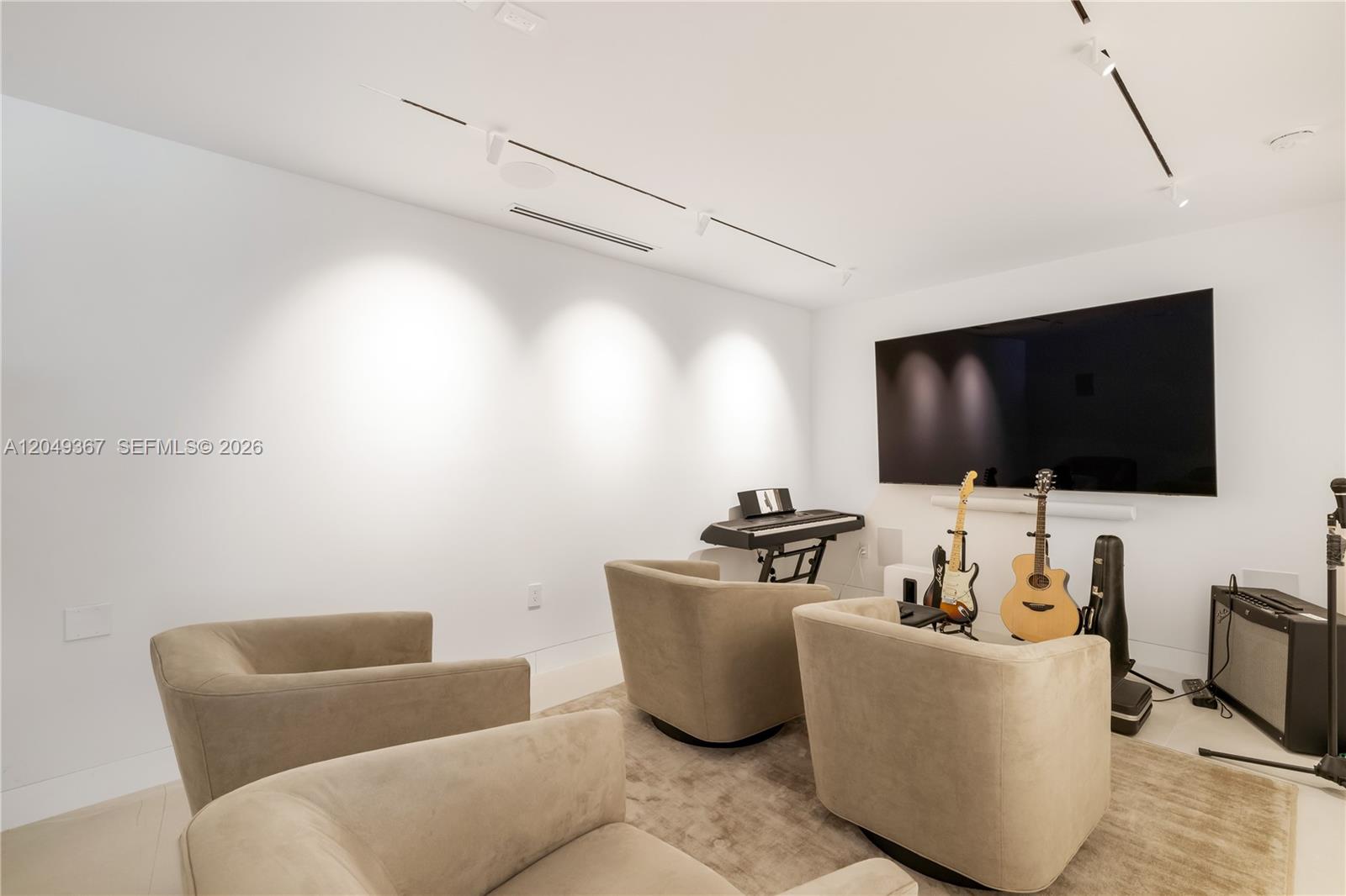 A modern media room features beige armchairs, musical instruments, and a large wall-mounted television — 7180 E Lago Dr, Coral Gables FL 33143, CORAL GABLES, FL