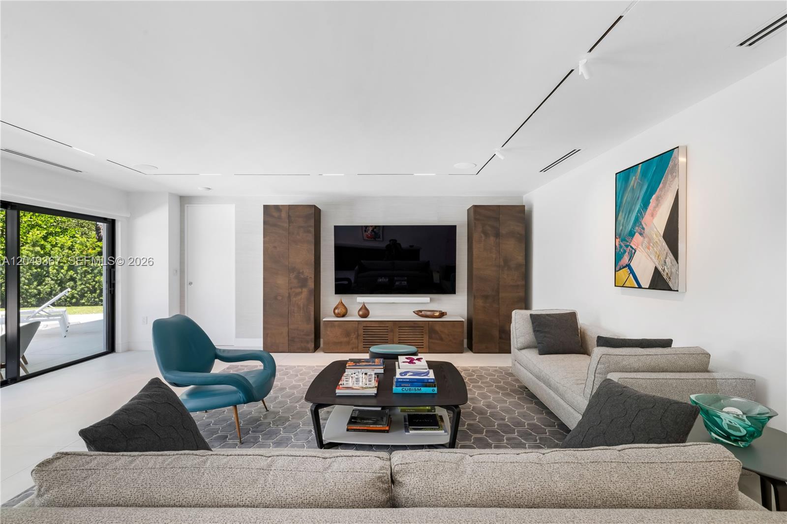 A modern living room features a large television, wood cabinetry, and a blue accent chair — 7180 E Lago Dr, Coral Gables FL 33143, CORAL GABLES, FL