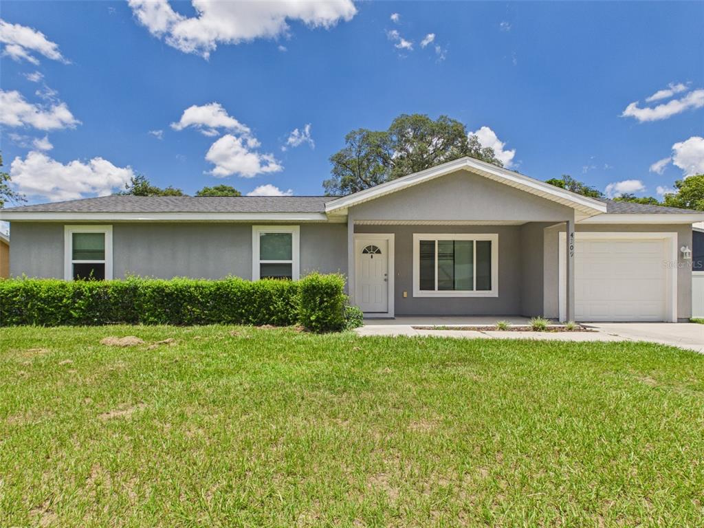 A single-story gray house with a white front door, garage, and a manicured hedge — 4309 SW 143RD LANE ROAD, OCALA, FL