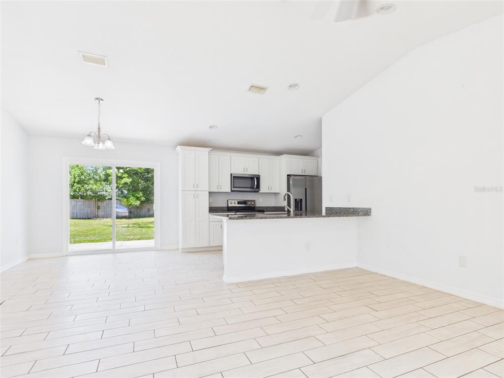 A bright kitchen with white cabinets and a breakfast bar overlooks a backyard through sliding doors — 4309 SW 143RD LANE ROAD, OCALA, FL