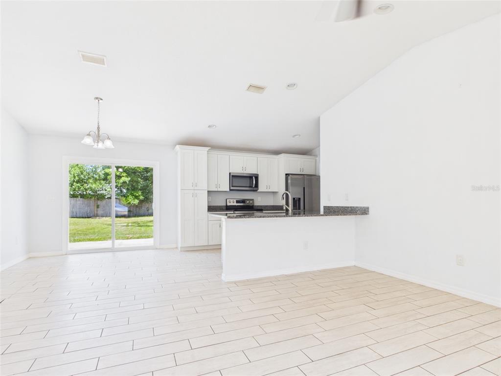 A bright kitchen and dining area features white cabinets, stainless appliances, and light tile flooring — 4309 SW 143RD LANE ROAD, OCALA, FL