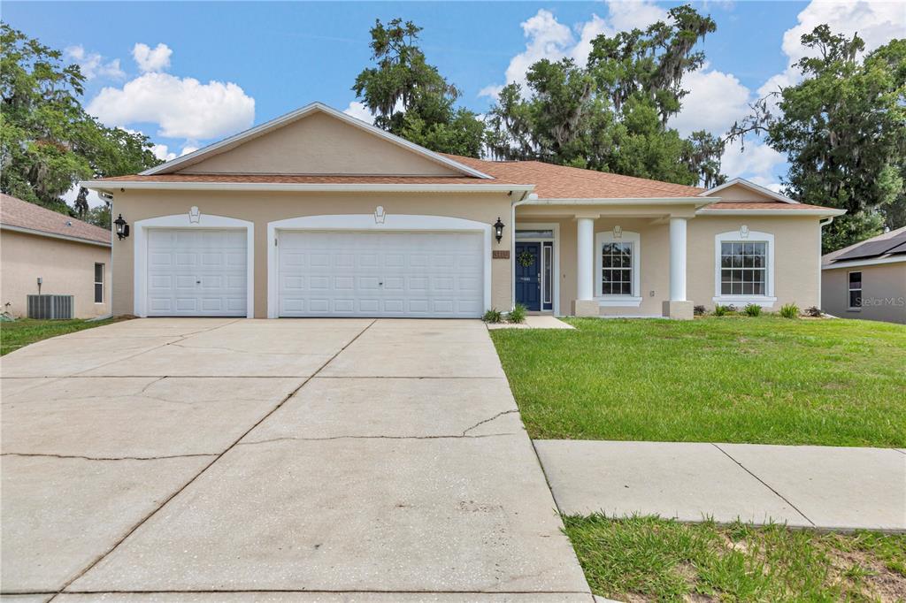 A single-story house with a beige stucco exterior, a three-car garage, and a front porch — 3115 NE 25TH STREET, OCALA, FL