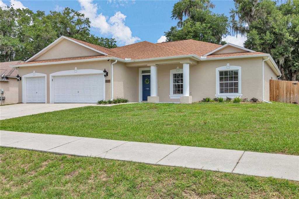 A single-story beige house with a two-car garage, a covered entryway, and a grassy lawn — 3115 NE 25TH STREET, OCALA, FL
