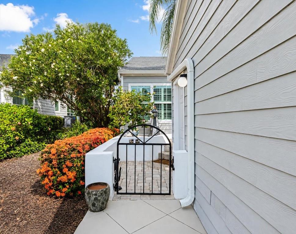 A black metal gate leads to a paved courtyard beside a gray-sided house — 1240 SPOONBILL LANDINGS CIRCLE, BRADENTON, FL